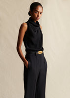 Model wearing black sleeveless draped neck top tucked into black pants, with a leather belt that has a gold fern leaf on it.