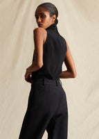 Model standing backwards wearing sleeveless black top tucked into black pants.