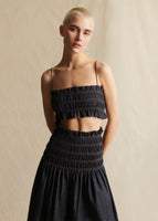 A model wears a navy blue chambray smocked crop top with thin straps, and a smocked skirt in matching fabric.