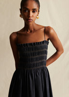 A close-up image of a model wearing a navy blue dress, with thin straps at shoulders and elastic smocking at neckline.