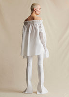 Image of a model standing backwards wearing a white off the shoulder top with white flare pants.