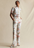 Model standing forwards wearing a white ground floral short sleeved top tucked into matching flare leg pants. 