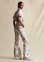 A model standing sideways wearing a white ground floral flared pant, styled with a white ground floral short sleeved printed top.