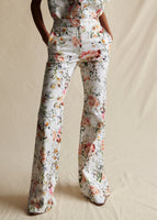 A close up of a model wearing a white ground floral flared pant. 