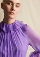 A close-up image of a model wearing a purple chiffon dress with ruffle collar.