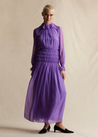 A model wearing a purple chiffon long dress that has smocking at the waist.