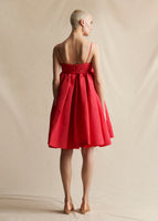 A model standing backwards wearing a red silk short dress with cami straps.