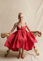 Image of a model sitting down wearing a red pleated dress with thin straps.