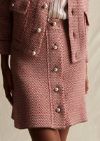 A close-up of a pink and white tweed knit mini skirt with pearl buttons on the center,