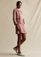 A side view of a model wearing a pink and white tweed knit jacket that has pearl buttons, with a matching pink and white tweed knit mini skirt that also has pearl buttons.