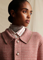 Close-up of a model from chest up wearing a pink and white tweed knit jacket with a collar, and pearl buttons. 