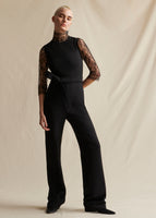 A model wearing a black sleeveless jumpsuit with fabric belt tie at the waist.