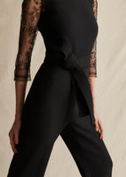 A close up image of a model wearing a black sleeveless jumpsuit with a fabric belt tie at the waist.
