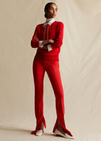 A model wearing  red sweater, layered over a red and white striped top. Styled with red flare pants that have a slit near the ankle. Her arms are crossed across her chest.