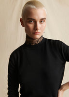 Close up image from chest up of a model wearing a black crewneck sweater with a black lace turtleneck.