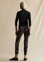 An image of a model standing backwards wearing a black floral printed cigarette pant and black crewneck sweater.