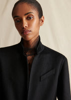 Close up image from the chest up of a model wearing a black coat over a black lace turtleneck.
