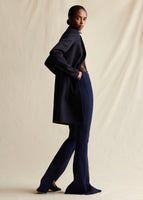 A side view of a model wearing a navy blue cashmere mid length coat styled over navy blue flare pants.