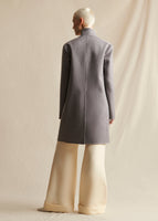 Image of a model standing backwards, wearing a gray cashmere coat styled with ivory wide leg pants.