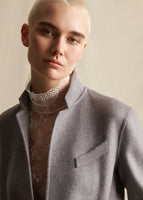 A close-up image of a model wearing a grey cashmere coat styled over an ivory lace turtleneck.