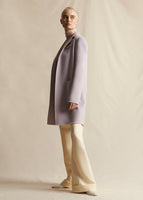 A model stands sideways wearing a lilac coat, styled with ivory wide leg pants.