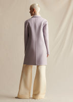 A model stands backwards wearing a lilac coat with ivory wide leg pants.