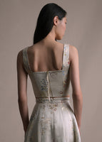 A back-facing image of a model wearing a cropped champagne jacquard tank with floral detail and a zipper with a long easily accessible zipper paired with matching skirt/