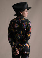 A back-facing image of a model wearing a black long sleeve shirt with collar, thin bow, and multicolor printed flowers with matching pants.