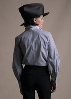 A back-facing image of a model wearing a striped navy and white long sleeve blouse with an asymmetrical tie-front worn with hat and black pants.