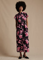 Model is wearing the Shirt Dress in Printed Poplin in black with a pink floral design. The dress is ankle-length, short sleeved and belted with buttons from the collar to the bottom hem.