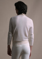 Cropped image of a model facing backwards wearing a white crewneck sweater and white pants.