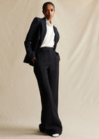 Model wearing a black blazer over an ivory silk top, with black pants and her hands in the pocket of the pants.