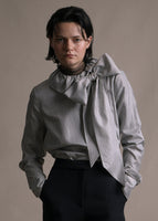 Model wearing a long sleeve blouse with high neckline in stripe shirting with a tied bow at the front neck and worn with black pants.