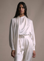 Model wearing long sleeve silk charmeuse blouse with an asymmetrical wrap front in ivory with matching pants. 