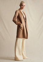 A model wearing a camel mid-length coat, layered over an ivory lace turtleneck. Styled with ivory wide leg pants.