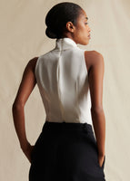 Model standing backwards, wearing a sleeveless ivory silk top tucked into black pants.