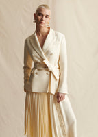 Image of a model standing forwards wearing ivory double breasted blazer with an ivory pleated skirt.