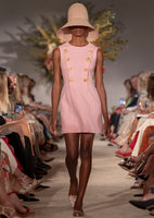 Model is facing forward wearing a classic Adam Lippes rose-colored sheath dress, updated with decorative gold flower buttons.