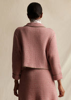 A model stands backwards wearing a red and white tweed knit cropped jacket and matching mini skirt