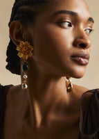 A close-up of a model wearing gold flower earrings with a green stone and crystal drop down.