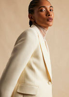 Cropped in image of a model standing sideways wearing an ivory blazer.