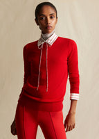 A model wearing a red crew neck sweater with a red and white striped shirt layered underneath, and red pants.