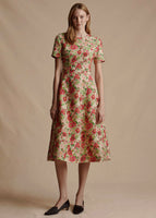 Image of a model standing forwards wearing a printed short sleeved midi length dress. It is printed with a pink and pistachio colored floral.