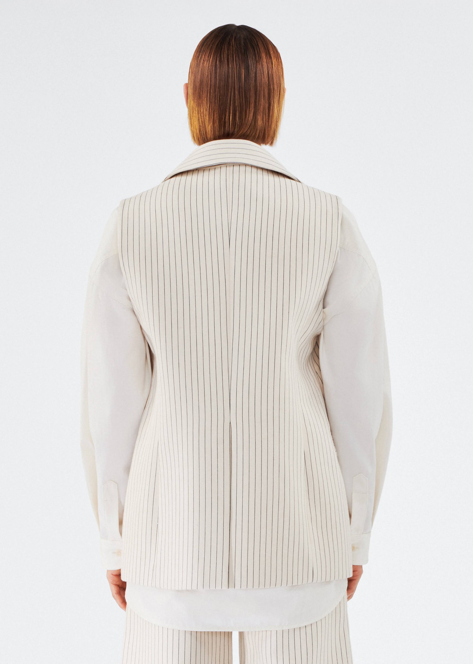 back of model wearing the callen vest by adam lippes in pinstripe twill layered over a top 