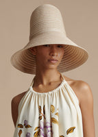 Close-up image of a model wearing a sand colored tall hat with an ivory printed halter dress.