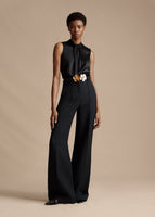 Model standing forwards wearing a black sleeveless silk top tucked into black wide leg pants.