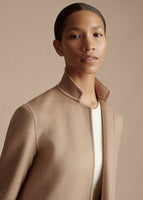 A close up cropped image of a model wearing a camel collared coat.