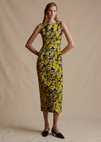 Model is wearing the Ophelia Dress in Printed Silk Wool. The Dress is midi length and sleeveless with a fitted waist. The floral print is yellow and black.