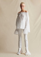 Image of a model standing forwards wearing a white bonded neoprene pant and a white off the shoulder top.