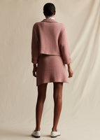 A back view of a model wearing a pink and white tweed knit jacket and matching short skirt.